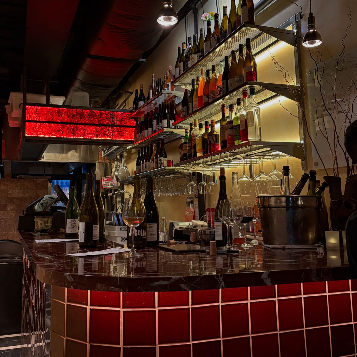 The bar at Malavita with lit bottle shelves and a red tiled counter